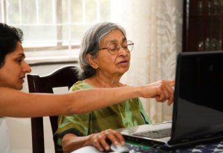 caregiver teaching elderly woman on how to use computer